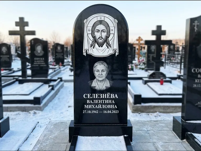 Памятник с гравировкой иконы: небольшая скромная одиночная стела с именной иконой — золочёный нимб на образе, аккуратный участок с газоном, работа «Ковалёв» в Барнауле