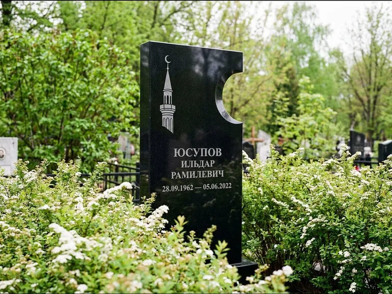 Мусульманский памятник с гравировкой мечети: стела с боковым вырезом в форме полумесяца — гравировка минарета с полумесяцем, низкие кусты спиреи в цвету, работа «Юсупов» в Барнауле
